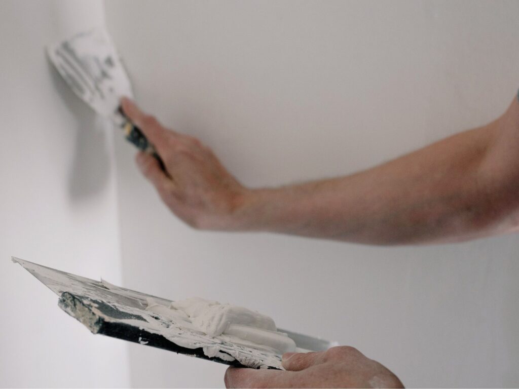 Una espátula aplicando masilla de reparación sobre una pared