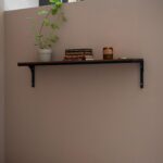 Balda de madera colgada en la pared con escuadras metálicas, libros y una planta