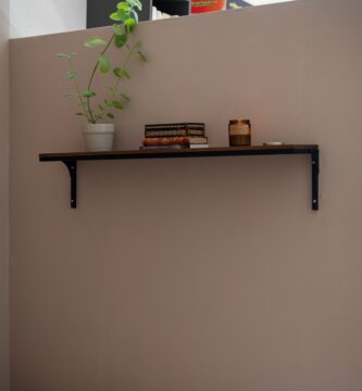 Balda de madera colgada en la pared con escuadras metálicas, libros y una planta