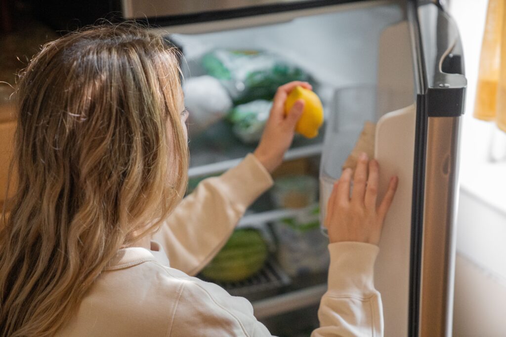Una mujer coge un limón del interior de un frigorífico con la puerta abierta