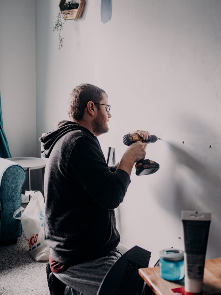 Hombre taladrando una pared interior junto a dos agujeros ya marcados